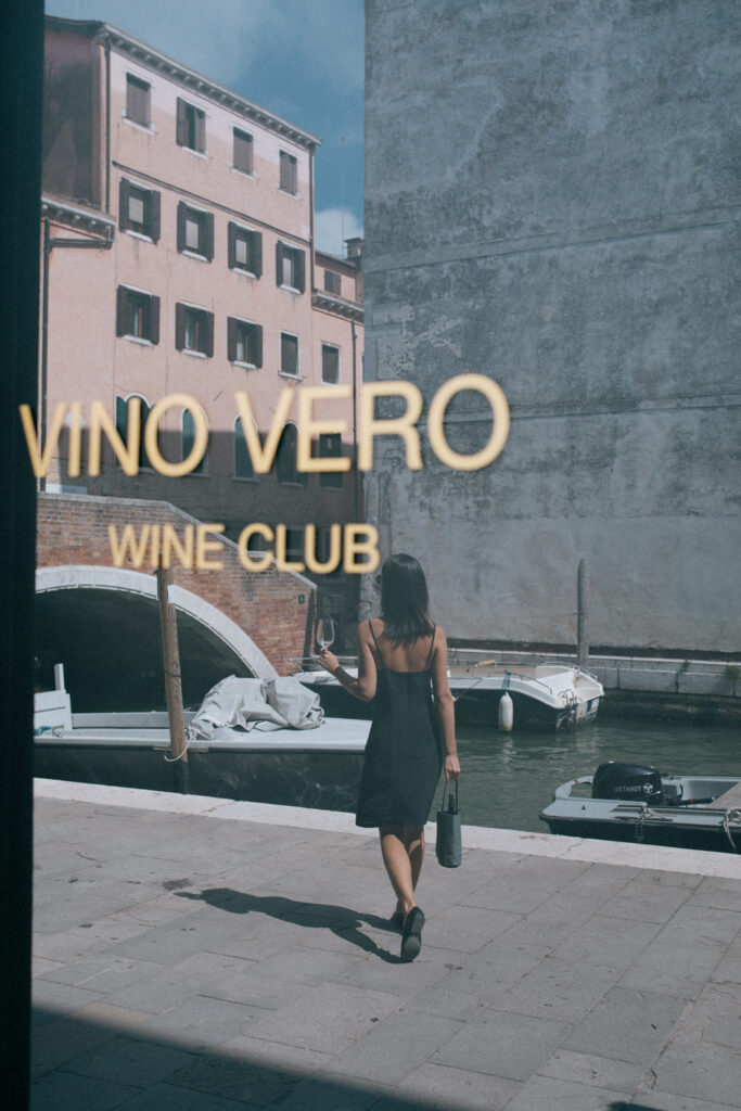 Grey linen wine cooler and bottle holder carried by a woman in front of a shop window in the streets of Venice