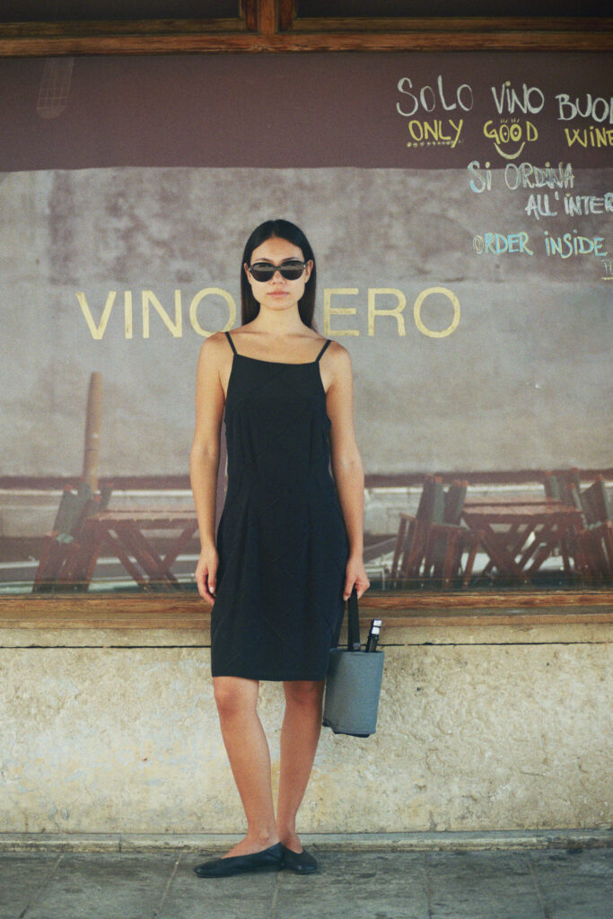 Grey linen wine cooler and bottle holder carried by a woman in front of a shop window in the streets of Venice